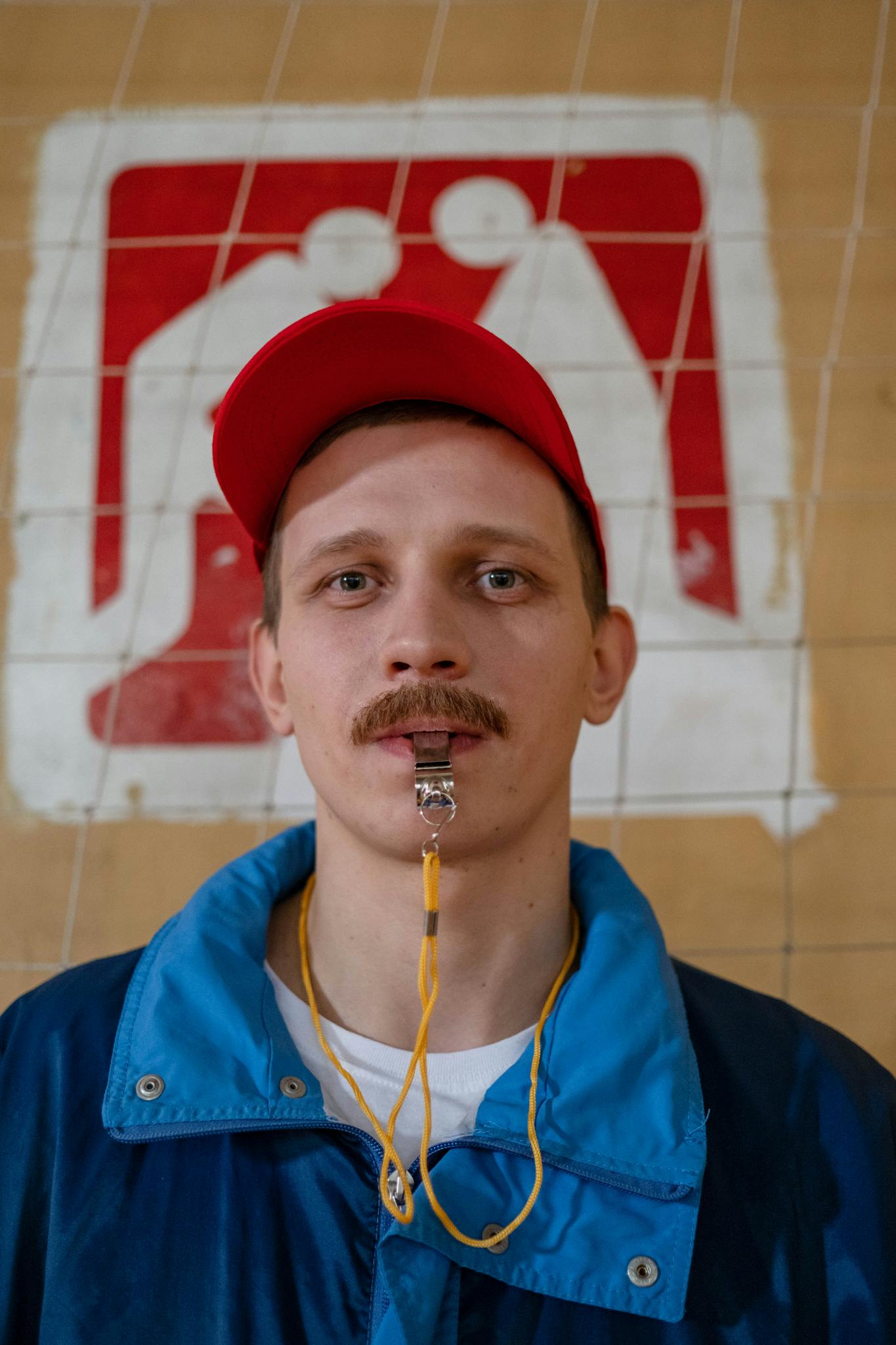 Close-up of a caucasian male coach with a whistle, standing in a gym setting.